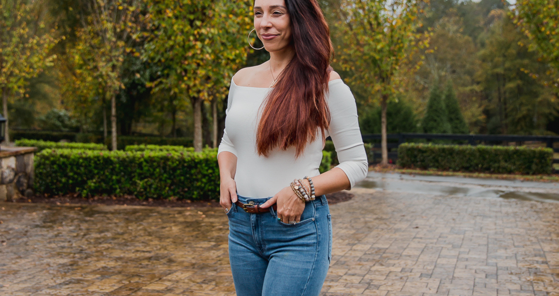 CeCe standing in front of a garden wearing a grey off-the-shoulder top